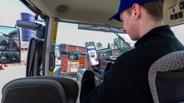Kund sitter i traktor med en telefon i handen och letar efter kontaktuppgifter till DeLaval rådgivare